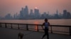 Una mujer trota con un perro a lo largo del río Hudson poco después del amanecer, mientras la neblina y el humo causados ​​por los incendios forestales en Canadá se ciernen sobre el horizonte de Manhattan, en la ciudad de Nueva York, Nueva York, EEUU, 7 de junio de 2023.
