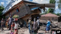 People walk next to a house destroyed by floods in the village of Nyamukubi, South Kivu province, in the Democratic Republic of Congo, May 6, 2023. 