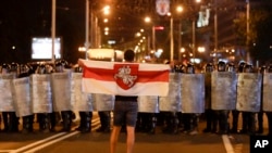 FILE - A protester holds an old Belarusian national flag as he stands in front of police line during a rally after the Belarusian presidential election in Minsk, Belarus, Aug. 9, 2020.