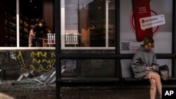 A commuter waits for a bus in front of a liquor store damaged in Russian drone attacks in Kyiv, Ukraine, Aug. 2, 2023.