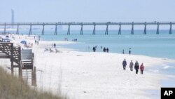FILE - People walk along the shoreline in Navarre Beach, Fla., on March 27, 2013.