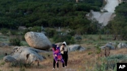 The border wall separating Jacumba Hot Springs, Calif., and Mexico is seen in the background as Chinese migrants walk to await processing by US authorities May 8, 2024, near Jacumba Hot Springs, Calif. 