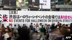 Orang-orang menunggu di depan papan bertuliskan "Tidak ada acara Halloween di jalan-jalan Shibuya" di Shibuya Crossing di distrik Shibuya, Tokyo, 27 Oktober 2023. Pemerintah setempat meminta masyarakat untuk tidak merayakan Halloween di sana. (Philip FONG / AFP)