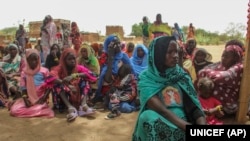 In this photo provided by UNICEF, refugees rest under a tree to protect themselves from the sun and heat after crossing into the village of Koufroun, near the Chad-Sudan border, in Chad, April 27, 2023. (UNICEF via AP)
