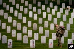 FILE - A member of the 3rd U.S. Infantry Regiment places flags in front of each headstone for "Flags-In" at Arlington National Cemetery in Arlington, May 25, 2023, to honor the nation's fallen military heroes ahead of Memorial Day.