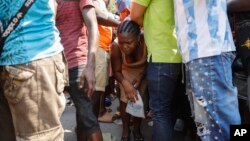 A woman squeezes through a human chain of volunteers as she is given the go-ahead to pass through for a plate of free food, at a shelter for families displaced by gang violence in Port-au-Prince, Haiti, March 14, 2024.