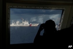 A crew member of Philippine coast guard patrol vessel BRP Malabrigo uses binoculars to monitor the Chinese coast guard ship as it runs beside them near the Second Thomas Shoal, at the South China Sea, April 23, 2023.