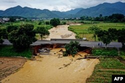 Orang-orang berjalan melewati jembatan yang rusak pasca badai di Longyan, provinsi Fujian, China timur, 17 Juni 2024. (CNS / AFP)