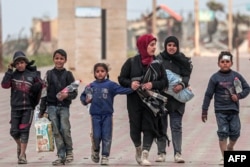 Displaced Palestinians fleeing from the vicinity of Gaza City's Shifa Hospital walk along the coastal highway as they arrive at the Nuseirat refugee camp in the central Gaza Strip, March 18, 2024, amid battles between Israel and the militant group Hamas.