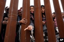 FILE - Migrants reach through a border wall for clothing handed out by volunteers, as they wait between two border walls to apply for asylum, in San Diego, May 12, 2023.