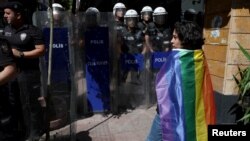 FILE - An activist stands near riot police who prevent activists from marching in a pride parade, which was banned by local authorities, in central Istanbul, June 26, 2022.