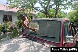 Seorang pria membersihkan abu vulkanik di kaca depan mobilnya usai Gunung Lewotobi Laki-Laki meletus di Klatanlo, Nusa Tenggara Timur pada 23 Desember 2023. (Foto: AFP/Putra Tulida) ​