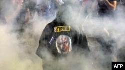A protester wearing a garment depicting the Israeli prime minister walks through smoke as relatives and supporters of Israelis taken hostage by Palestinian militants in Gaza in the October 7 attacks demonstrate in Tel Aviv on May 26, 2024