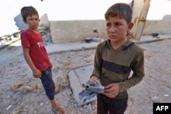 A boy holds a piece of metal as he stands with another youth after Russian airstrikes hit an abandoned water pumping station in Syria's rebel-held northwest, Aug. 23, 2023.