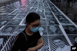 FILE - A pedestrian passes smiling portraits on display as part of the installation titled "Inside Out: Harbour and the City" created by French artist JR in Hong Kong, April 26, 2023.