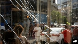 People are seen through a broken window next to the scene of an explosive drone attack in Tel Aviv, Israel, July 19, 2024. Yemen's Houthi rebels claimed responsibility for a drone believed to have exploded above Tel Aviv early Friday, leaving one dead.