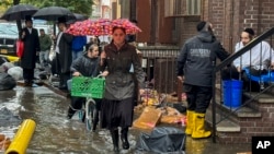 Pedestrians walk along a flooded sidewalk, Sept. 29, 2023, in the Brooklyn borough of New York. A potent rainstorm swamped the New York metropolitan area, shutting down swaths of the subway system, and flooded some streets and highways.