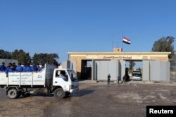 Egyptian cleaning workers are seen in front of the Rafah crossing from the Egyptian side, while trucks carrying humanitarian aid for Palestinians await for it to open to enter Gaza, in Rafah, Egypt, Oct. 19, 2023.