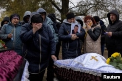 Relatives mourn at the coffins of Iryna Kharbaka and Oleksandr Khodak, who were killed in a Russian missile attack, amid Russia's ongoing invasion of Ukraine, at the village cemetery, in the village of Hroza, near Kharkiv, Ukraine, Oct. 9, 2023.