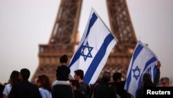 Supporters of Israel hold flags as they protest following Hamas' biggest attack on Israel in years, in Paris, France, Oct. 9, 2023, with the Eiffel Tower in the background.