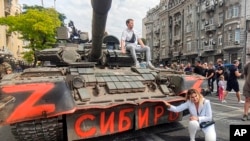 In this image taken from video, a woman poses for a photo at a Russian armored vehicle, with writing reading 'Siberia,' parked in a street in Rostov-on-Don, Russia, June 24, 2023. 