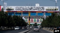FILE - Commuters drive under a banner placed by Taliban authorities, near the Kabul airport, Aug. 30, 2022. Taliban allegedly barred 100 female students from leaving Afghanistan for the United Arab Emirates in August 2023, where they were to enroll in university studies. 