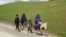 Mujeres afganas vestidas con burka montan en burro junto a niños en una carretera cerca de la aldea de Shah Mari en el distrito de Argo, provincia de Badakhshan, Afganistán, el 1 de mayo de 2024.