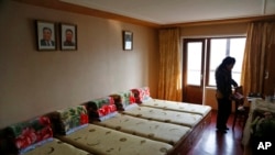 FILE - An employee stands inside a bedroom at a dormitory provided for textile factory workers as portraits of the late North Korean leaders Kim Il Sung and Kim Jong Il hang above the beds in Pyongyang, North Korea, Jan. 30, 2019.