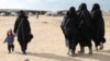 FILE - A woman holds a child's hand in the al-Hol camp, Syria, Jan. 8, 2020. 