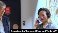Chinese Australian journalist Cheng Lei, right, talks on the phone as Australia's Minister for Foreign Affairs, Penny Wong, watches at Tullamarine Airport in Melbourne, Oct. 11, 2023. 