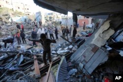 Warga Palestina berdiri di dekat sebuah bangunan yang hancur akibat pemboman Israel di Rafah, Jalur Gaza, 24 November 2023. (Foto: AP)