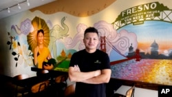 FILE - David Rasavong stands by a mural depicting his family's journey from Laos to San Francisco and then to Fresno, in his restaurant Love & Thai in Fresno, Calif. on Dec. 20, 2023. 