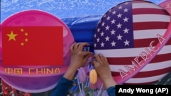 Seorang pedagang memajang dekorasi bunga di antara lingkaran yang diselimuti bendera China dan Amerika di Beijing pada 13 Mei 2023. (Foto: AP/Andy Wong)