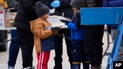 A young migrant receives food from the nonprofit Chi-Care, Jan. 11, 2024, in Chicago. Several city buses were parked in the area of 800 South Desplaines Street to house people in cold winter weather.