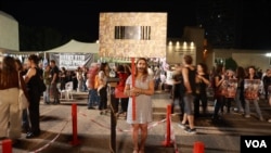 Israeli artist Hila Galili holds a sign with photos of the Israeli hostages held by Hamas with a mirror in the middle, meant to show that any citizen who looks in it could be among them, Nov. 4, 2023, in Tel Aviv. (Natasha Mozgovaya/VOA)