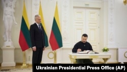 In this photo provided by the Ukrainian Presidential Press Office, Lithuania's President Gitanas Nauseda, left, watches Ukrainian President Volodymyr Zelenskyy sign the guest book in Vilnius, Lithuania, Jan. 10, 2024. (Ukrainian Presidential Press Office via AP)