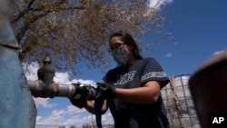 FILE - Raynelle Hoskie attaches a hose to a water pump to fill tanks in her truck outside a tribal office on the Navajo reservation, April 20, 2020, in Tuba City, Arizona.