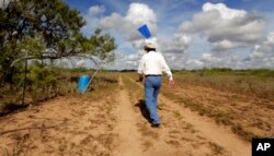 FILE - A rancher checks a 55-gallon tub he keeps filled with water jugs and marked by a flag on his ranch for migrants in need of water, near Falfurrias, Texas, Aug. 23, 2013.