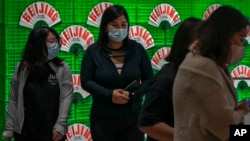 FILE - Women wearing face masks walk by fans on display inside a shopping mall in Beijing, May 30, 2023.