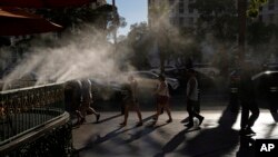 FILE - Pedestrians walk under cooling misters on a hot day in Las Vegas, Nevada, July 13, 2023. A recent study shows that intense and perpetual heat in the United States, Mexico and Central America is the result of human-caused climate change.  