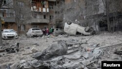 Residents stand near their apartment building and vehicles damaged during a Russian missile strike during Russia's attack on Ukraine, in Kharkiv, Ukraine, on Dec. 8, 2023.