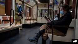 FILE - A woman wearing a face mask reads a book on a subway in Madrid, Spain, Jan. 20, 2022. Some areas of the country are reintroducing masks as COVID-19 cases rise. 