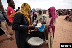 Sudanese people who fled the conflict in Geneina in Sudan's Darfur region, receive rice portions from Red Cross volunteers in Ourang on the outskirts of Adre, Chad, July 25, 2023.
