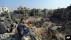 Seorang pria duduk di atas puing-puing, sedangkan orang-orang menyisir puing-puing yang menjadi target serangan udara Israel di kamp pengungsi Jabaliya di utara Jalur Gaza, 1 November 2023. (Foto: Abed Khaled/AP Photo)