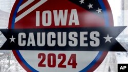 A man walks across the street below a sign for the Iowa Caucuses in downtown Des Moines, Iowa, Jan. 13, 2024. 