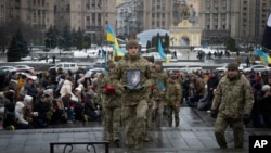People kneel as soldiers carry the coffin of Ukrainian serviceman and poet Maksym Kryvtsov — who was killed in a battle with Russian troops — during the funeral ceremony for Kryvtsov in St. Michael Cathedral in Kyiv, Ukraine, Jan. 11, 2024.