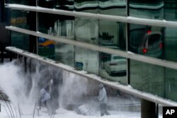 Men use snow blowers to clear a sidewalk in downtown Des Moines, Iowa, Jan. 13, 2024.