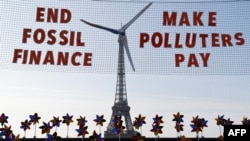 This photograph shows a replica of a wind turbine on a net reading 'End fossil finance, make polluters pay' as activists demonstrate against fossil finance on the Trocadero Plaza in Paris, on the eve of the Summit for a New Global Financial Pact. 