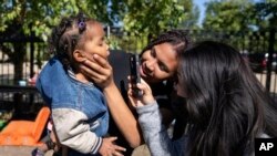 FILE - Anmani Rendon of Venezuela holds her 2-year-old daughter, Sofia Barragan, as med student Christina Guyn shines a light inside her mouth outside of the 12th District police station where migrants are camped, Oct. 7, 2023, in Chicago. 