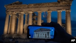 FILE - A woman holds up a mobile phone showing a digitally overlaid virtual reconstruction of the ancient Parthenon temple, at the Acropolis Hill in Athens, Greece on June 13, 2023.